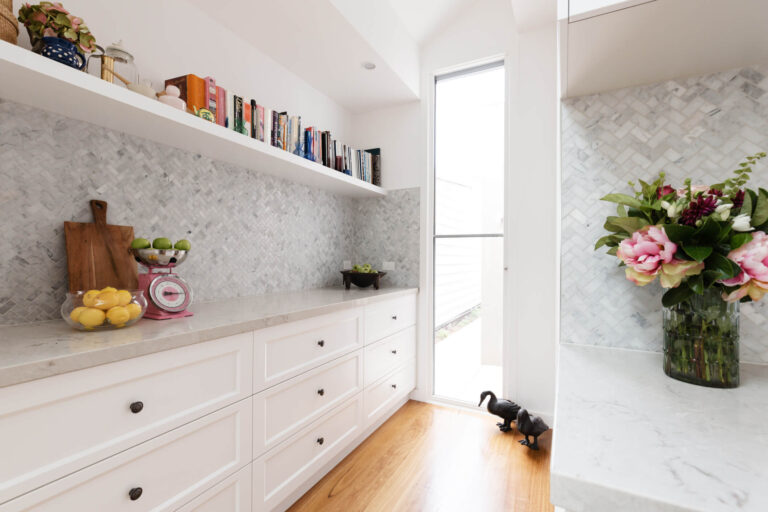 White kitchen pantry with marble splashback, open shelving, and timber flooring.