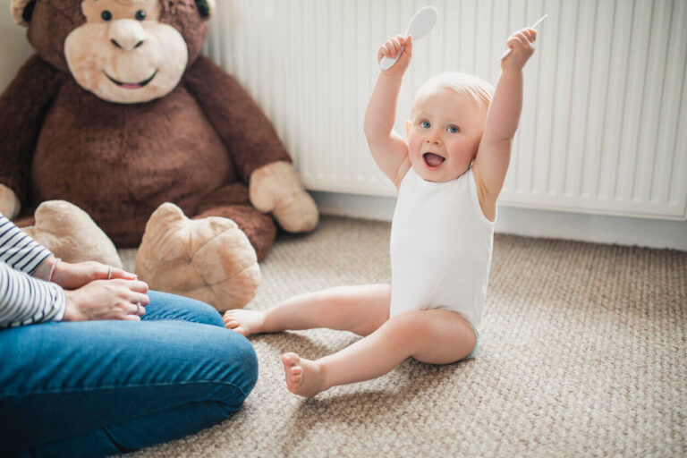 Baby sitting on soft carpet with a stuffed toy nearby