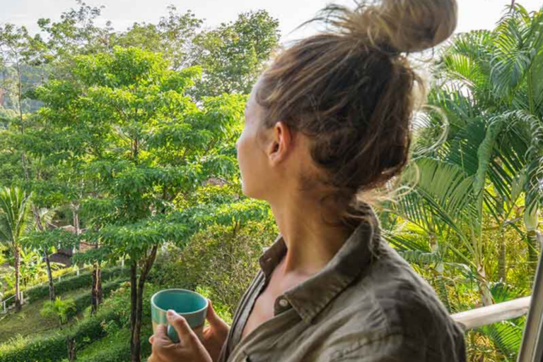 A woman holding a cup overlooking greenery.