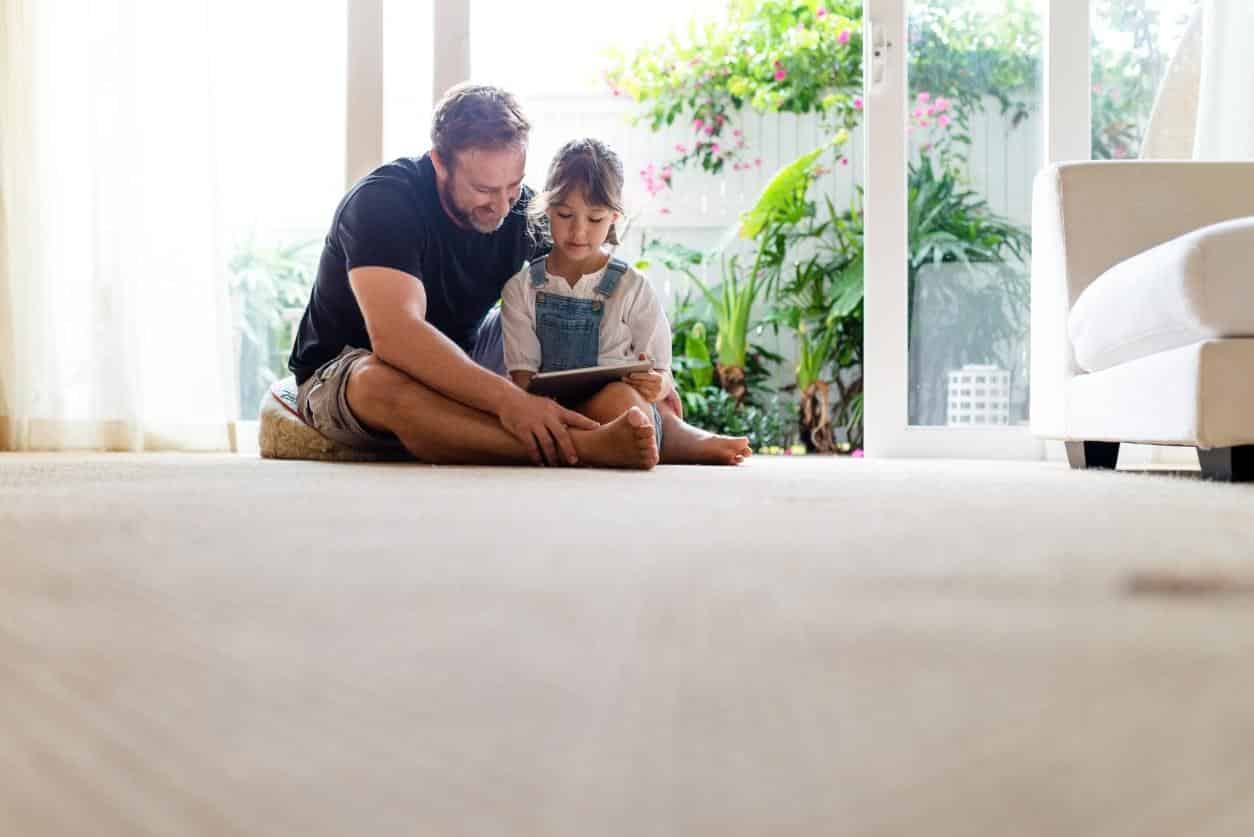 Father and child sitting on soft carpet in a bright living room.