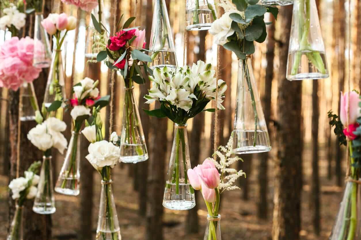 Hanging glass vases with fresh flowers in an outdoor setting.