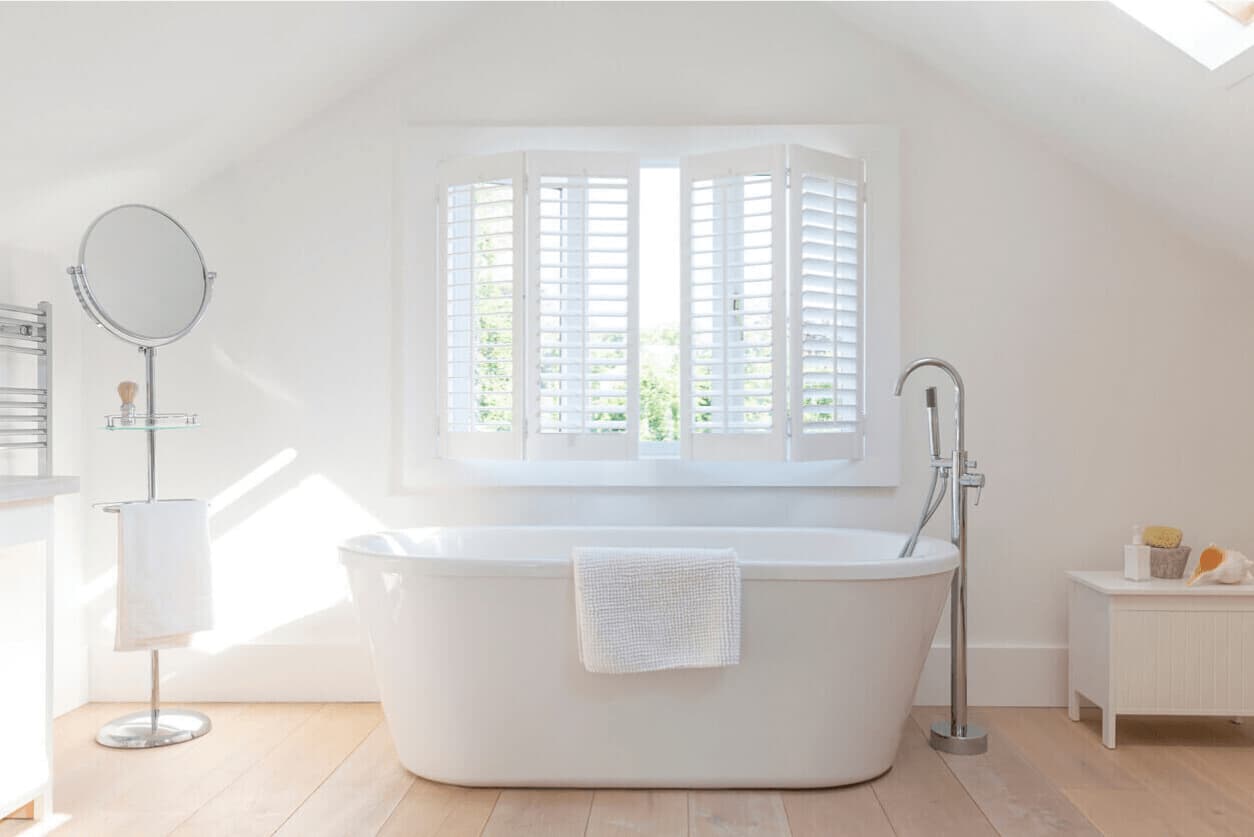 Bright bathroom with a freestanding bathtub and white plantation shutters allowing soft natural light
