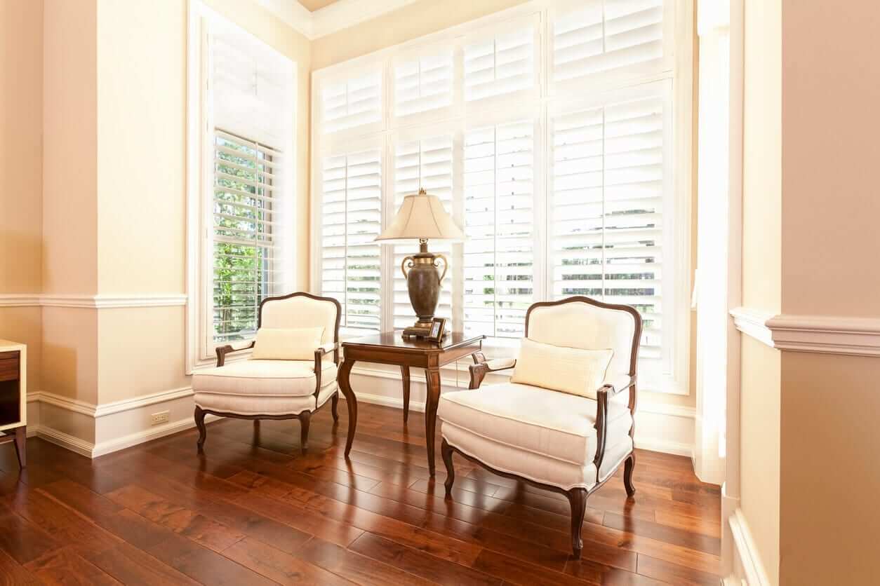 Living area with white plantation shutters, timber flooring and classic armchairs positioned by the bay window.