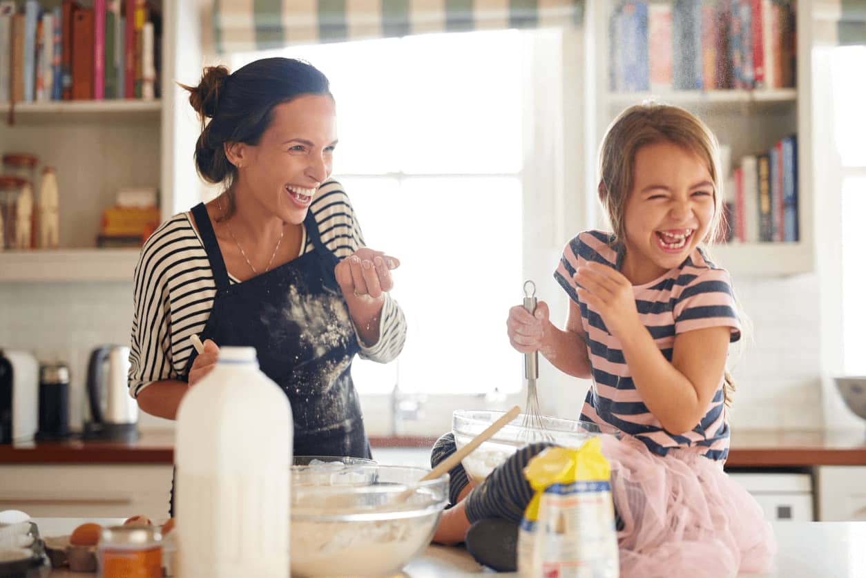 Adult and child laughing together while baking in the kitchen