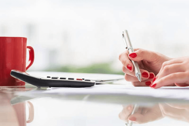 Person writing on paper beside a calculator and coffee mug