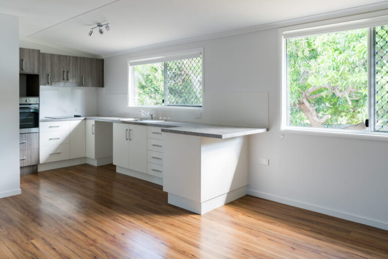 A kitchen with white base cabinet and timber-look flooring.