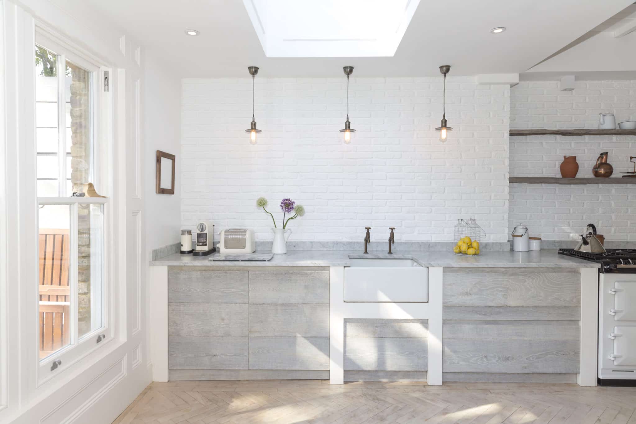 Kitchen with herringbone flooring, white brick wall and timber cabinetry.