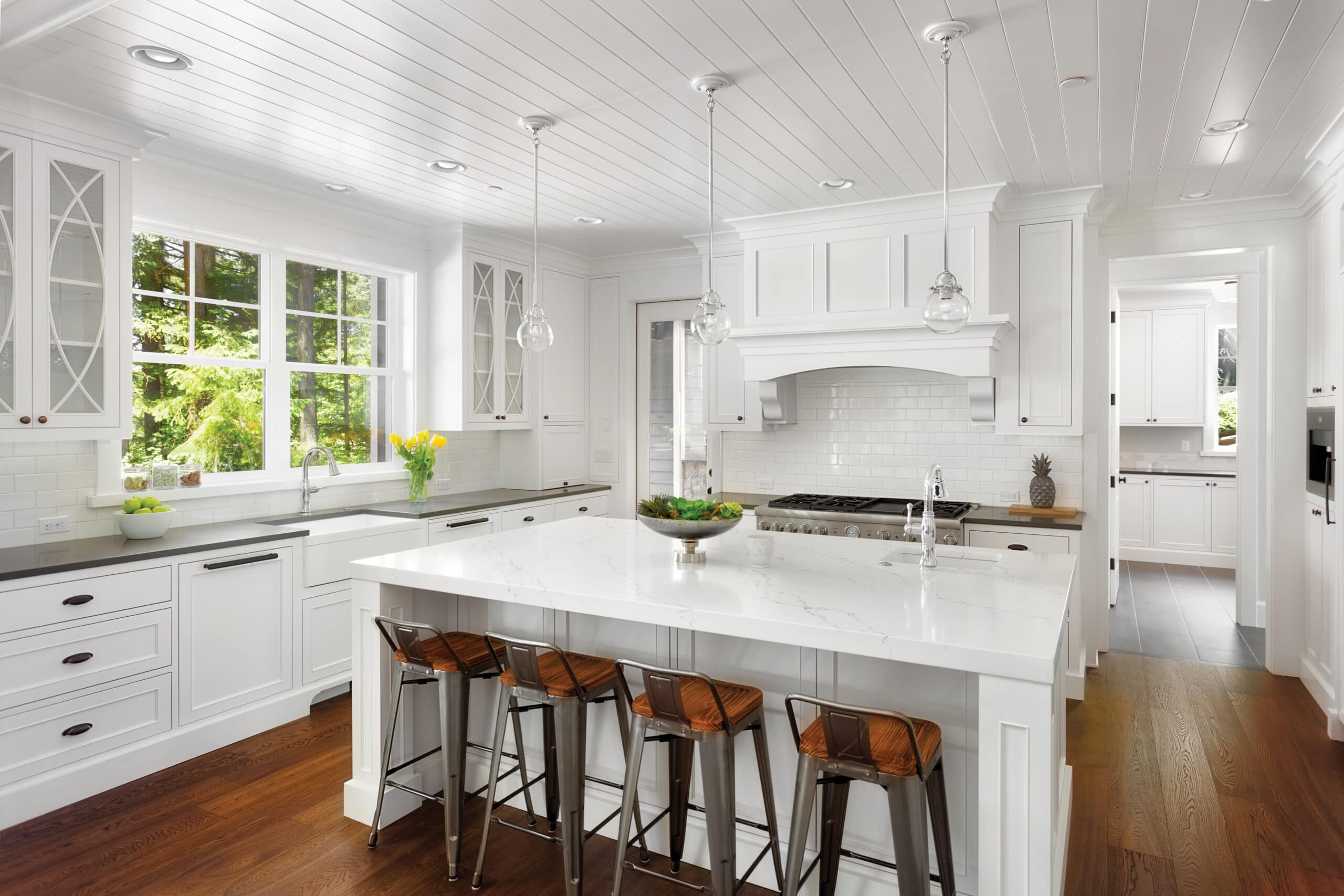 White kitchen with island bench, pendant lighting, and timber flooring.