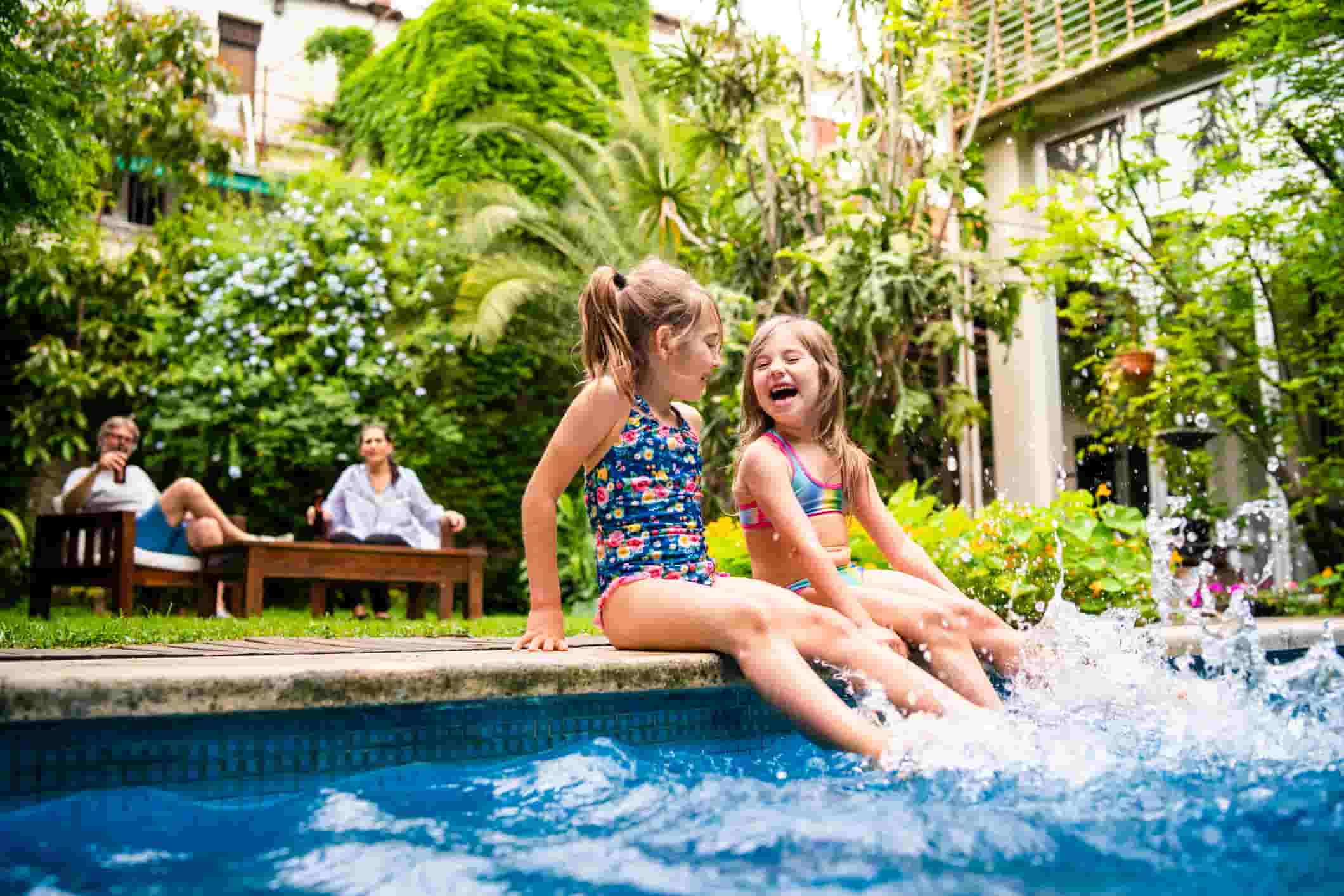 Children sitting by a swimming pool with water splashing.