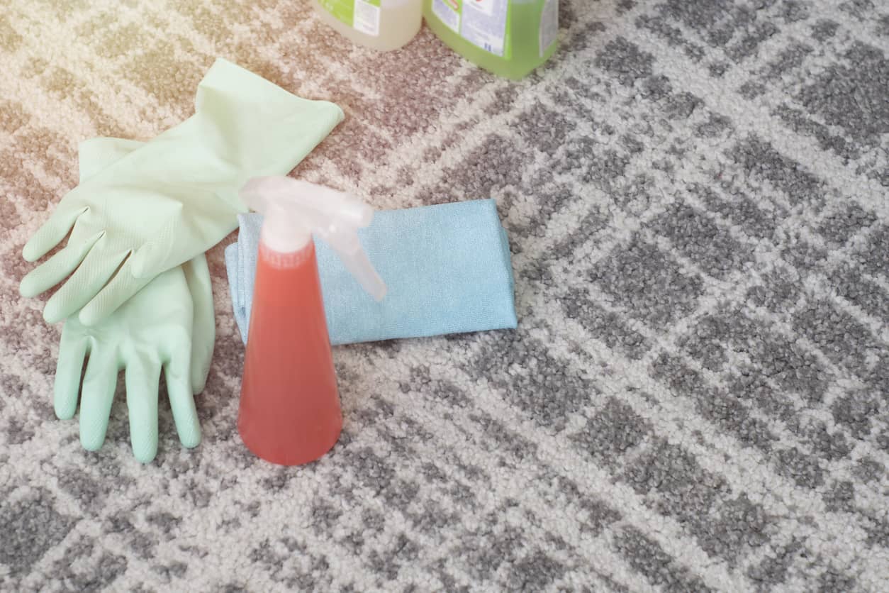 Carpet cleaning supplies including gloves, spray bottle and cloth placed on a patterned carpet.