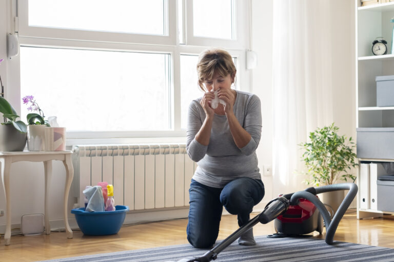 Woman kneeling on the floor sneezing while vacuuming carpet in a living room