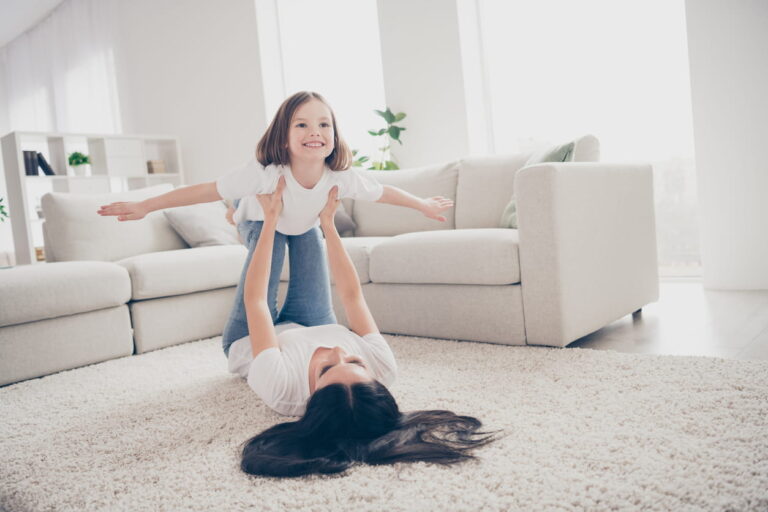 Child playing with parent on soft carpet in a living room.