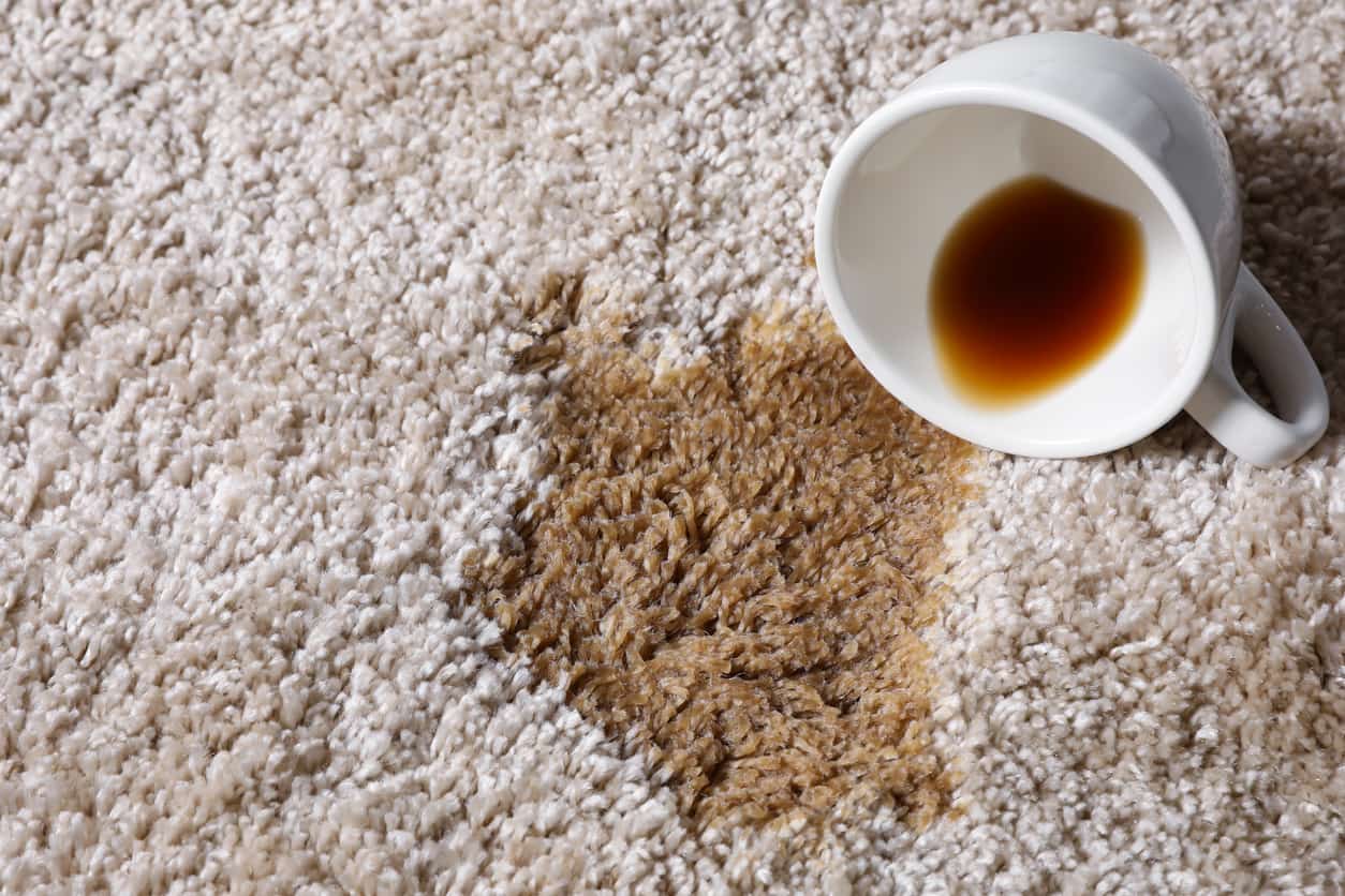 An overturned coffee cup spilling coffee on the carpet.