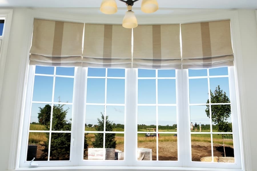 Bay window with roman shades and outdoor view.