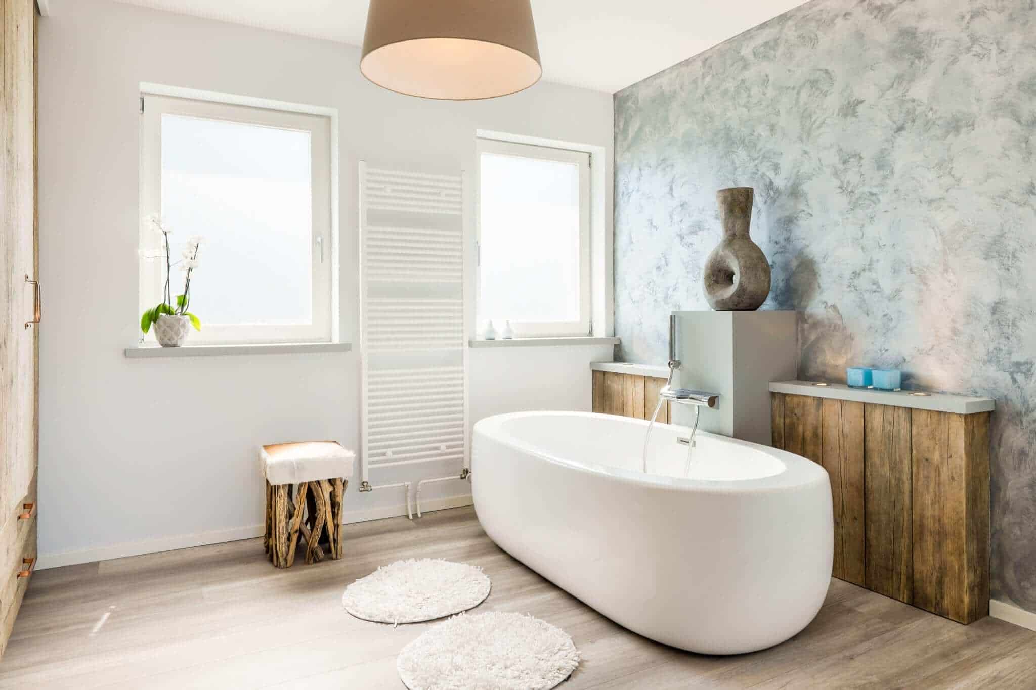 A bathroom featuring a grey accent wall, white bathtub and light-coloured timber-look flooring