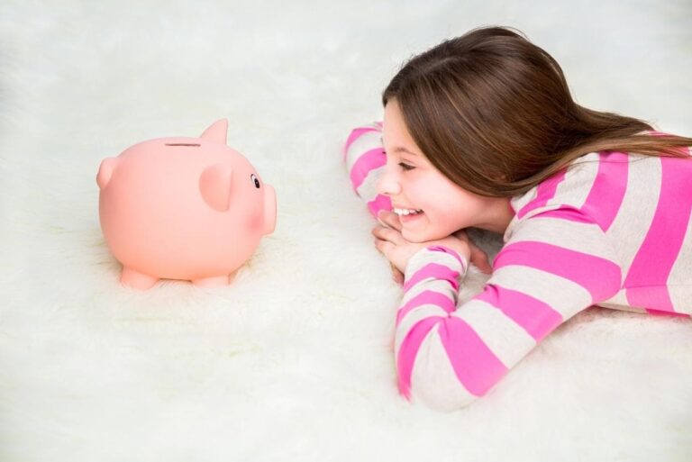 Child lying on soft carpet smiling at a pink piggy bank