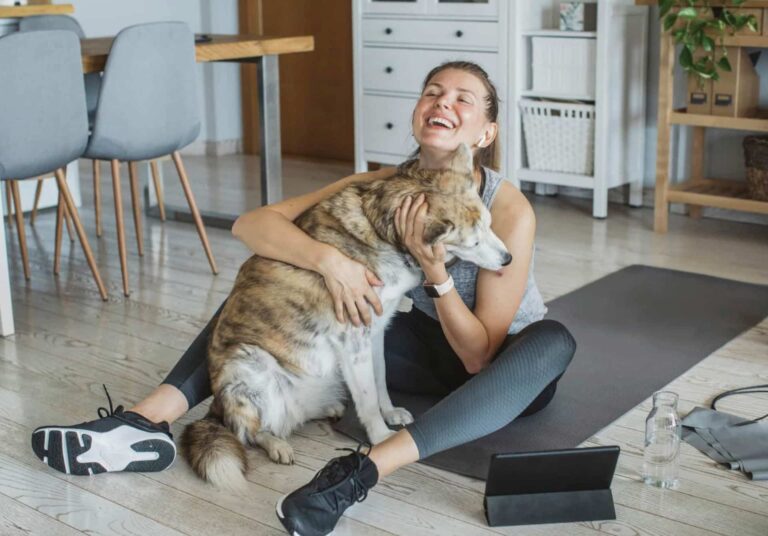 A homeowner sitting on hybrid flooring with her dog in a living area.