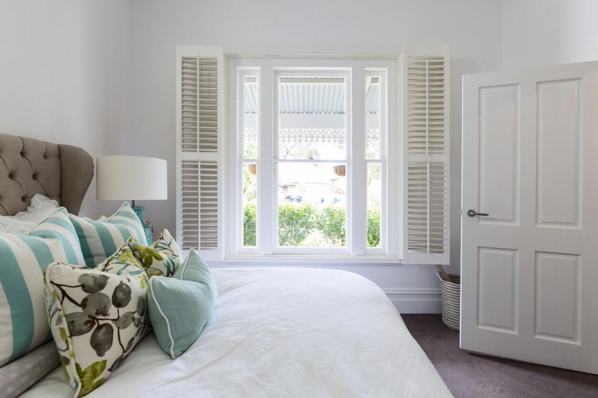 Bedroom with white plantation shutters framing a window and soft natural light filtering into the space.