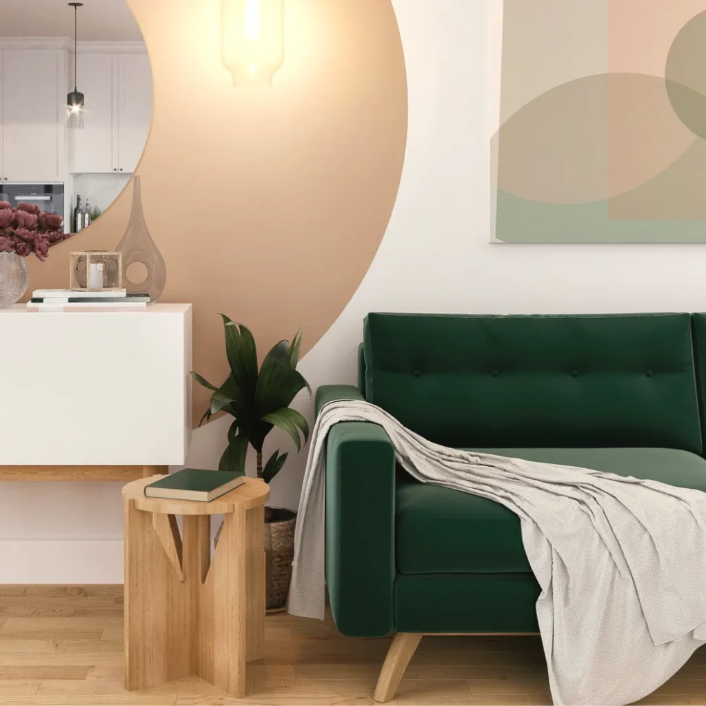 Contemporary bedroom featuring a dark green velvet sofa with white throw blanket, wooden side table with potted plant, white kitchen cabinetry, pendant light, and large curved wall art in warm peac...