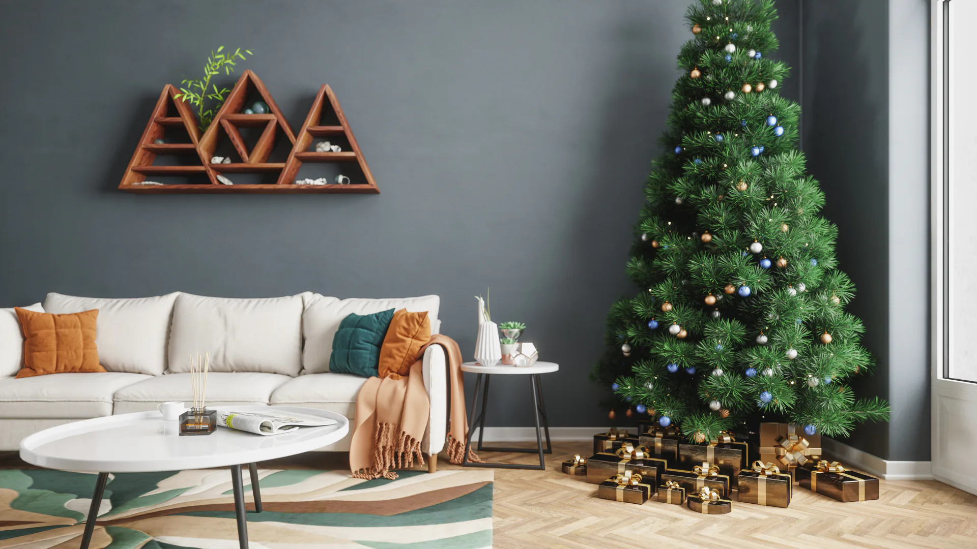 Contemporary living room with cream sectional sofa, geometric wooden triangle shelf on gray wall, decorated Christmas tree with gold and blue ornaments, wrapped gifts underneath, and modern white c...
