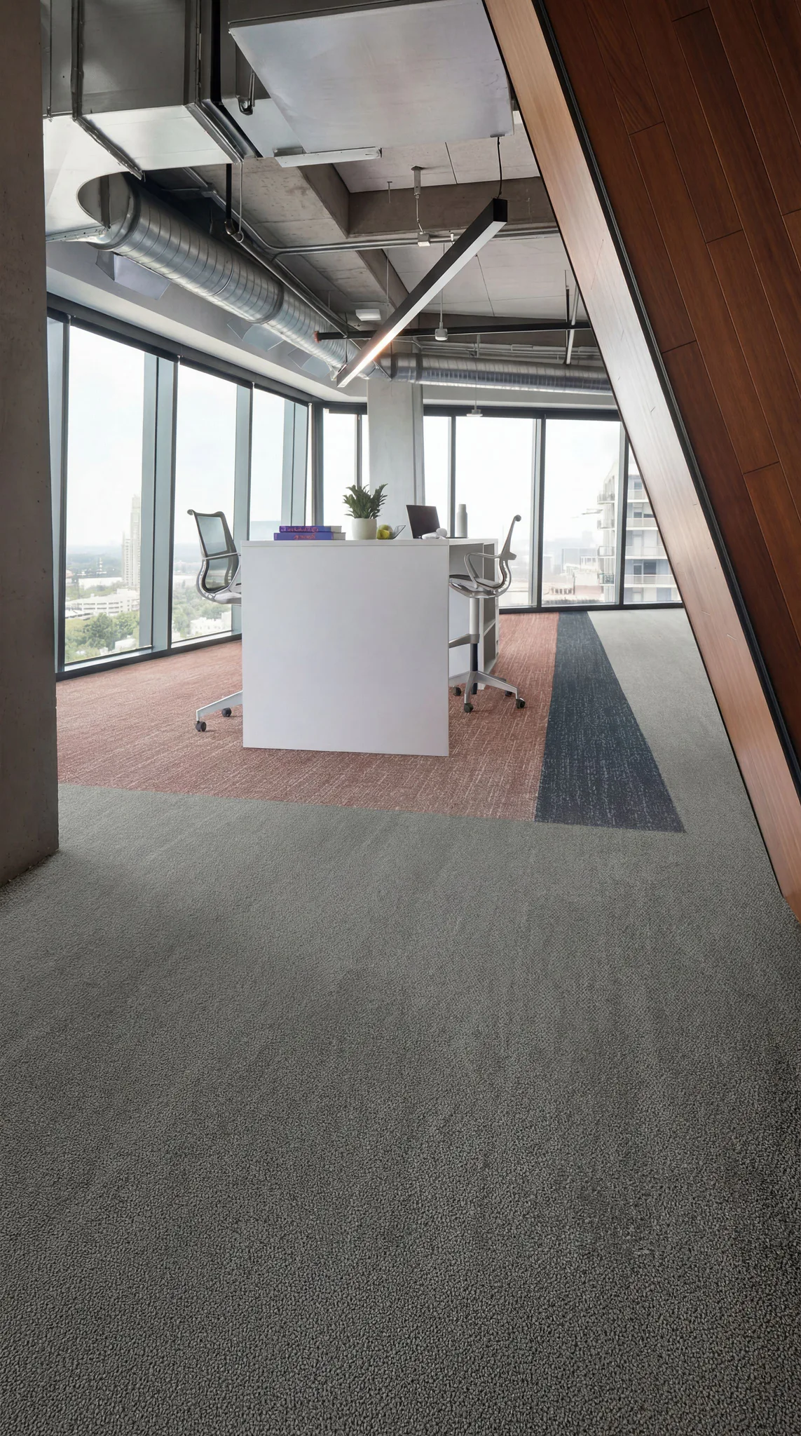 Modern office space with gray carpet flooring, white desk with mesh chairs, exposed ductwork ceiling, floor-to-ceiling windows overlooking city skyline, and wood accent paneling.