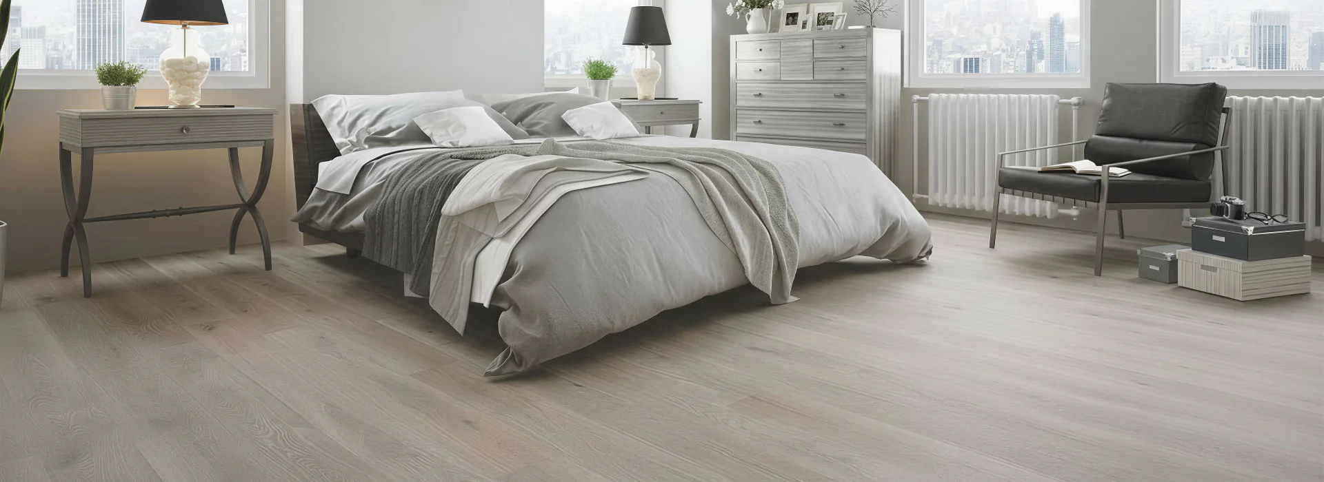 Spacious bedroom featuring light gray laminate flooring, queen bed with gray and white bedding, wooden nightstands with table lamps, dresser, reading chair, and floor-to-ceiling windows overlooking...