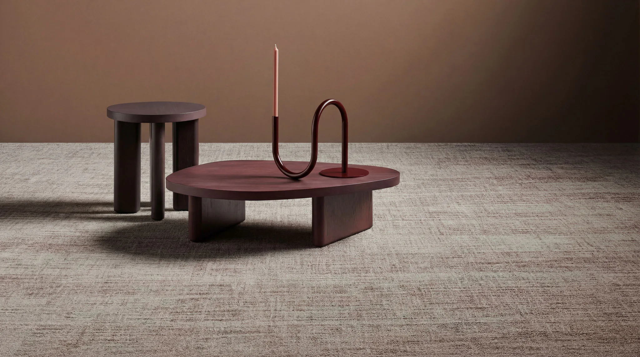 Modern minimalist furniture collection in deep burgundy and black tones arranged on neutral commercial carpet flooring, including round tables and decorative accessories.