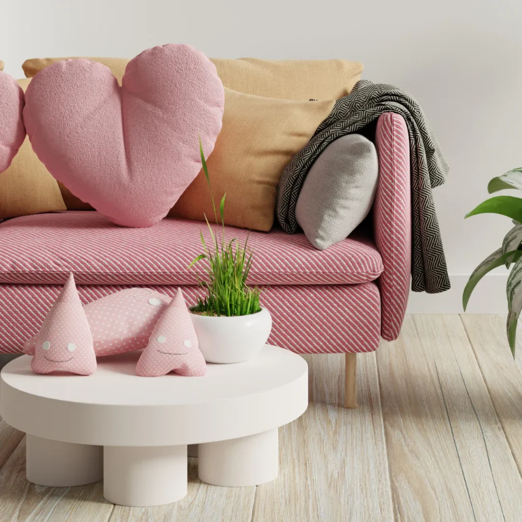 A pink striped sofa styled with heart-shaped pillows, patterned throws, geometric cushions, and a white round table displaying polka-dot decorative poufs and potted green grass plant.