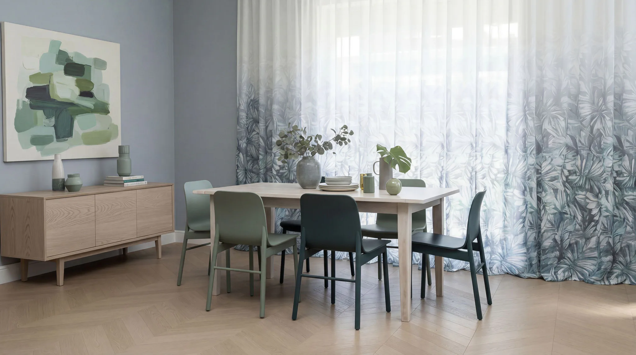 Contemporary dining room featuring light wood table with green chairs, wooden sideboard, abstract green artwork, and white sheer curtains with botanical palm print filtering natural light through l...