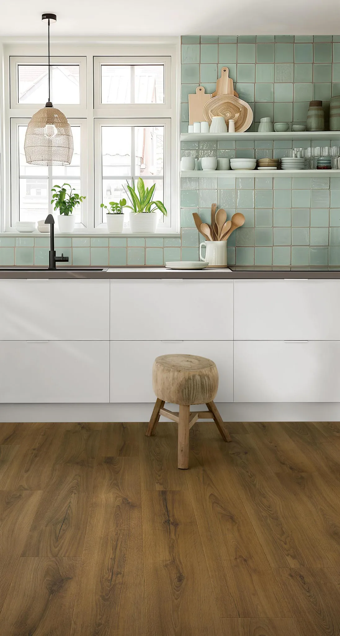 Modern kitchen interior featuring warm brown laminate wood flooring, white cabinets, sage green tile backsplash, wicker pendant light, and wooden stool