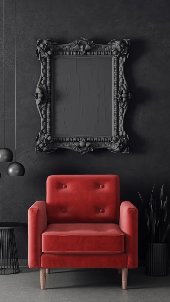 A vibrant red velvet armchair with button-tufted back and wooden legs positioned against a dark textured wall beneath an ornate black decorative mirror frame with baroque floral details.