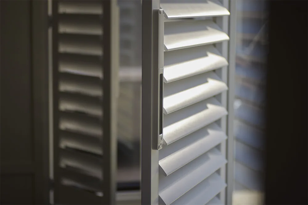 Close-up view of white plantation shutters with adjustable horizontal slats, showing multiple shutter panels with clean lines and premium finish quality